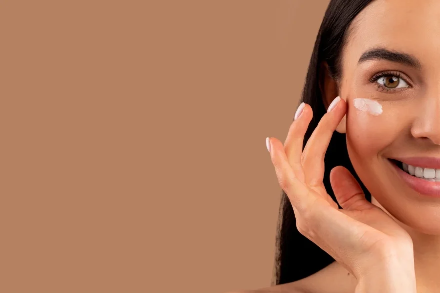 Smiling woman applying eye cream under her eye to treat and reduce the appearance of eyebags.